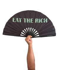 A black folding hand fan with the text 'EAT THE RICH' printed in mint green