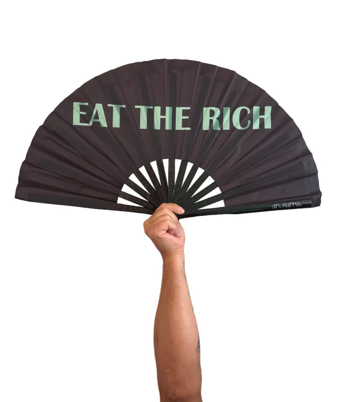 A black folding hand fan with the text 'EAT THE RICH' printed in mint green